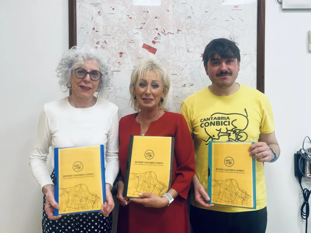Imagen donde parecen componentes de Cantabria ConBici, junto a la concejala del Ayuntamiento. Cada uno sostiene el informe de los puntos negros. La actitud hacia la cámara es sonriente y la fotografía muestra un tono de amistad.